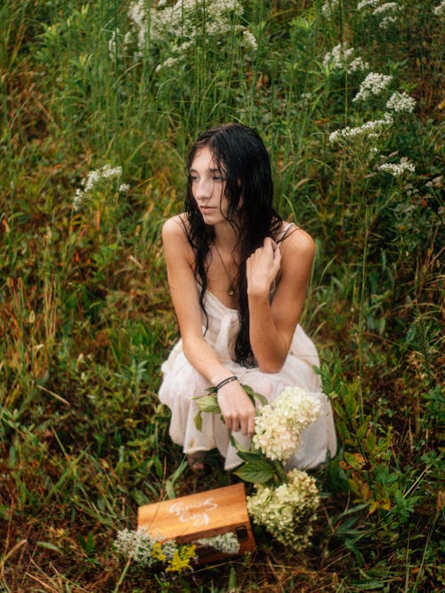 Woman in White Dress Squatting with Flowers on Meadow