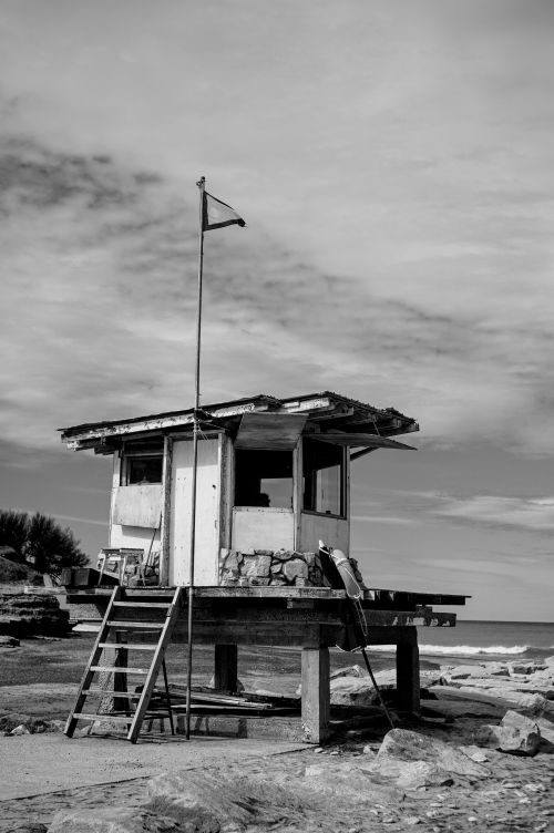 Free A black and white photo of an abandoned lifeguard hut on a rocky beach in Argentina. Stock Photo