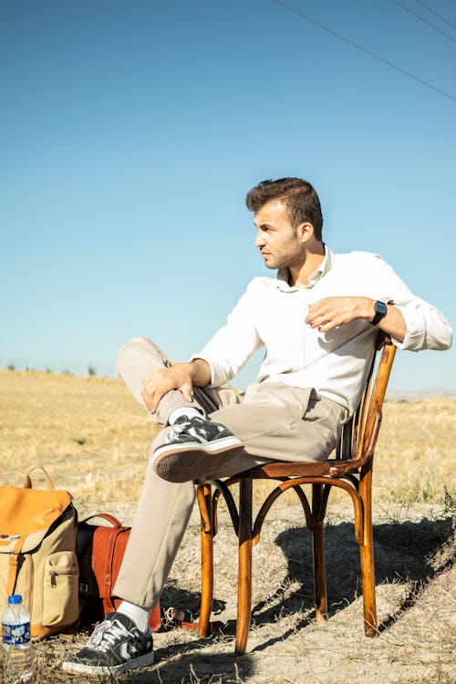 Man Sitting on a Chair in a Field Next to Luggage