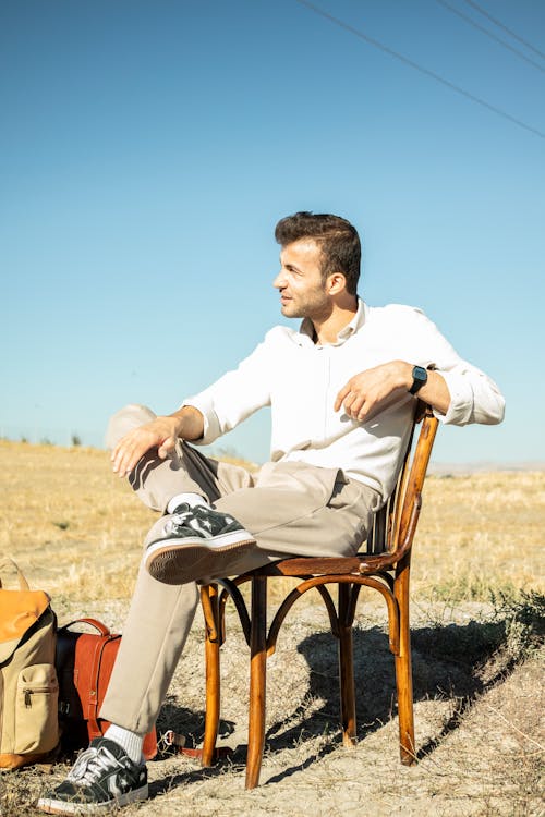 Man Sitting on a Chair in a Field Next to Bags