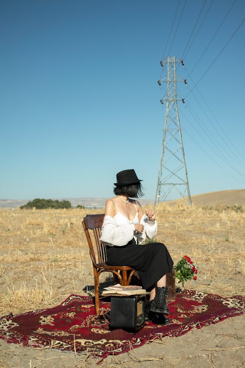 Woman in a Hat Sitting in a Chair on a Carpet Spread in a Field