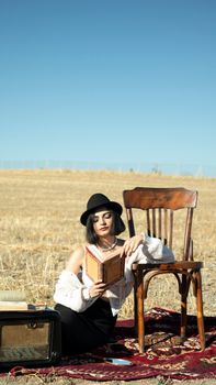 Woman in vintage attire reading outdoors in a rustic field, evoking a serene summer vibe.