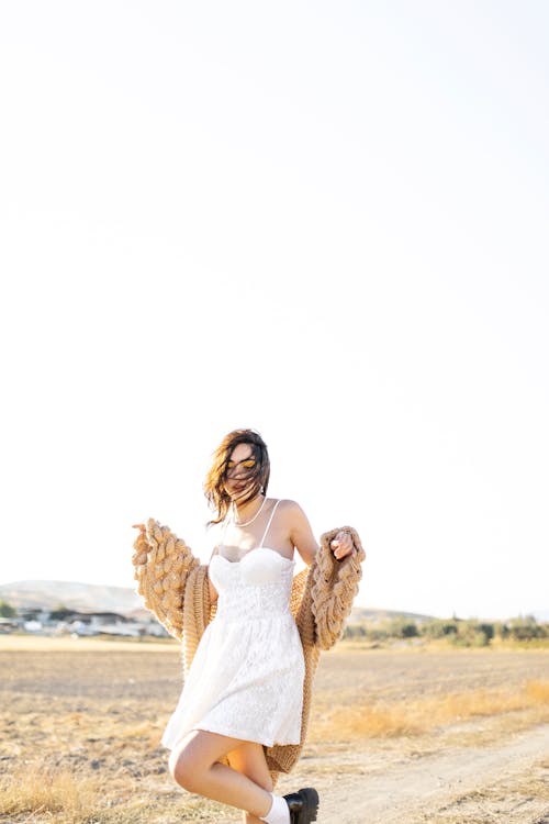 Model in a White Lace Sundress and a Long Beige Cardigan Dancing in a Field