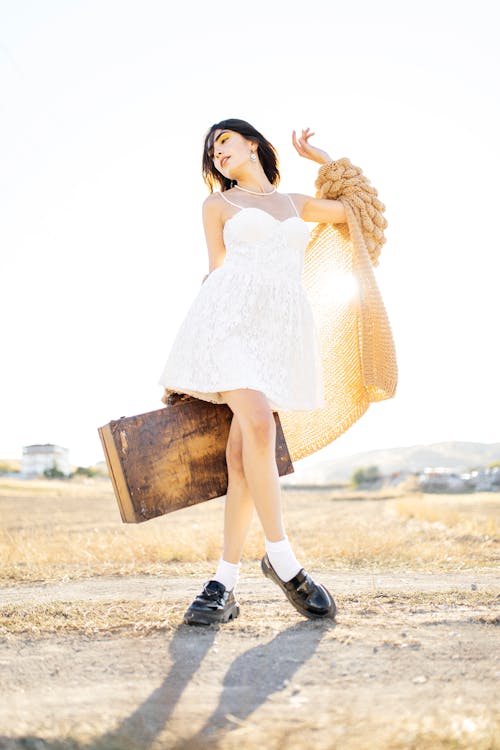 Young Woman in a Dress Posing Outside and Holding an Old Suitcase