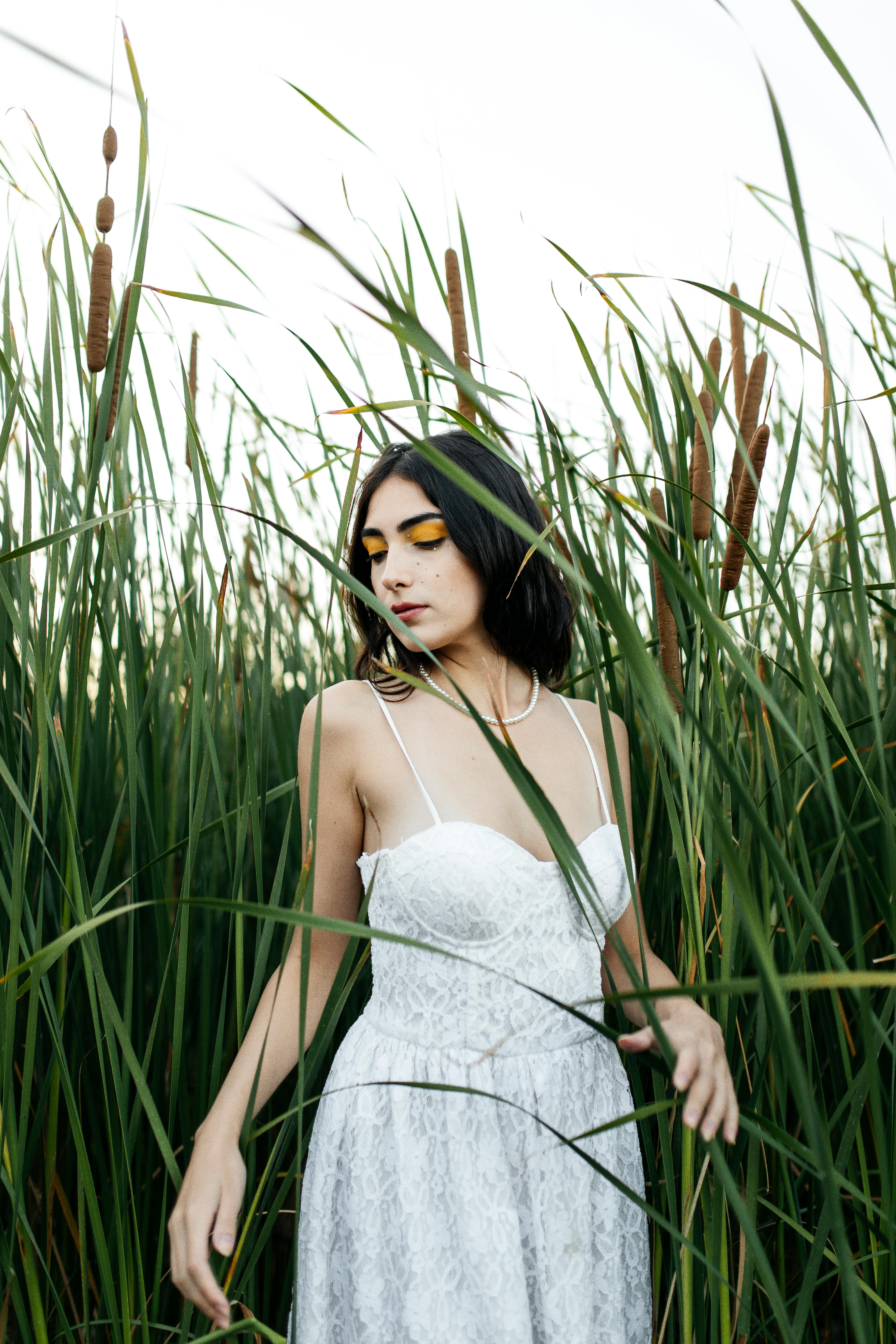 Young woman in a white dress posing amidst tall grass in a field, exuding a summer vibe.