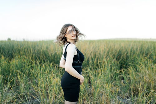 Young Woman in a Black Dress Standing on a Grass Field