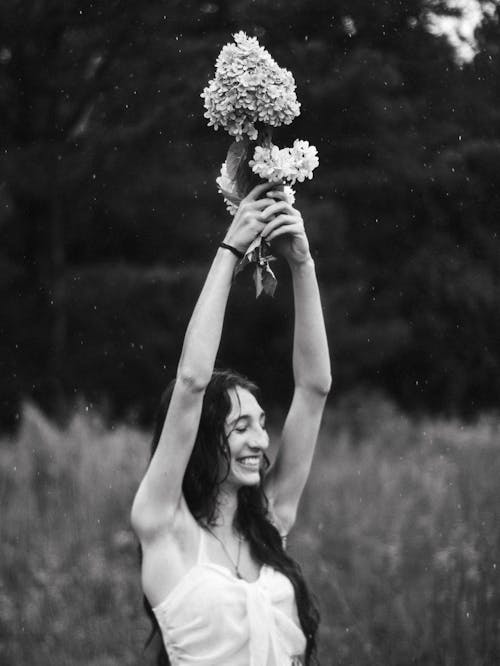 Smiling Woman Standing with Flowers in Raised Arms