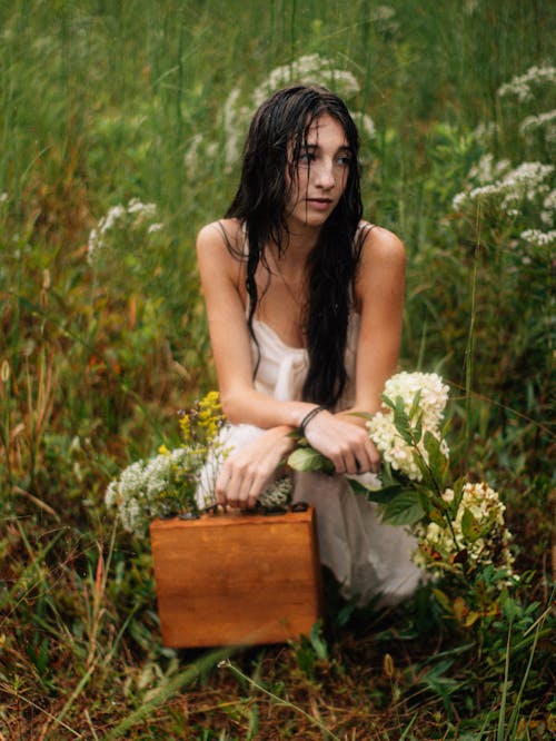 Brunette Woman Squatting with Suitcase on Meadow