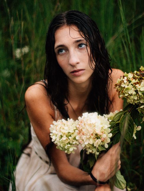 Portrait of a young woman with wet hair holding hydrangea flowers in a sunny meadow.
