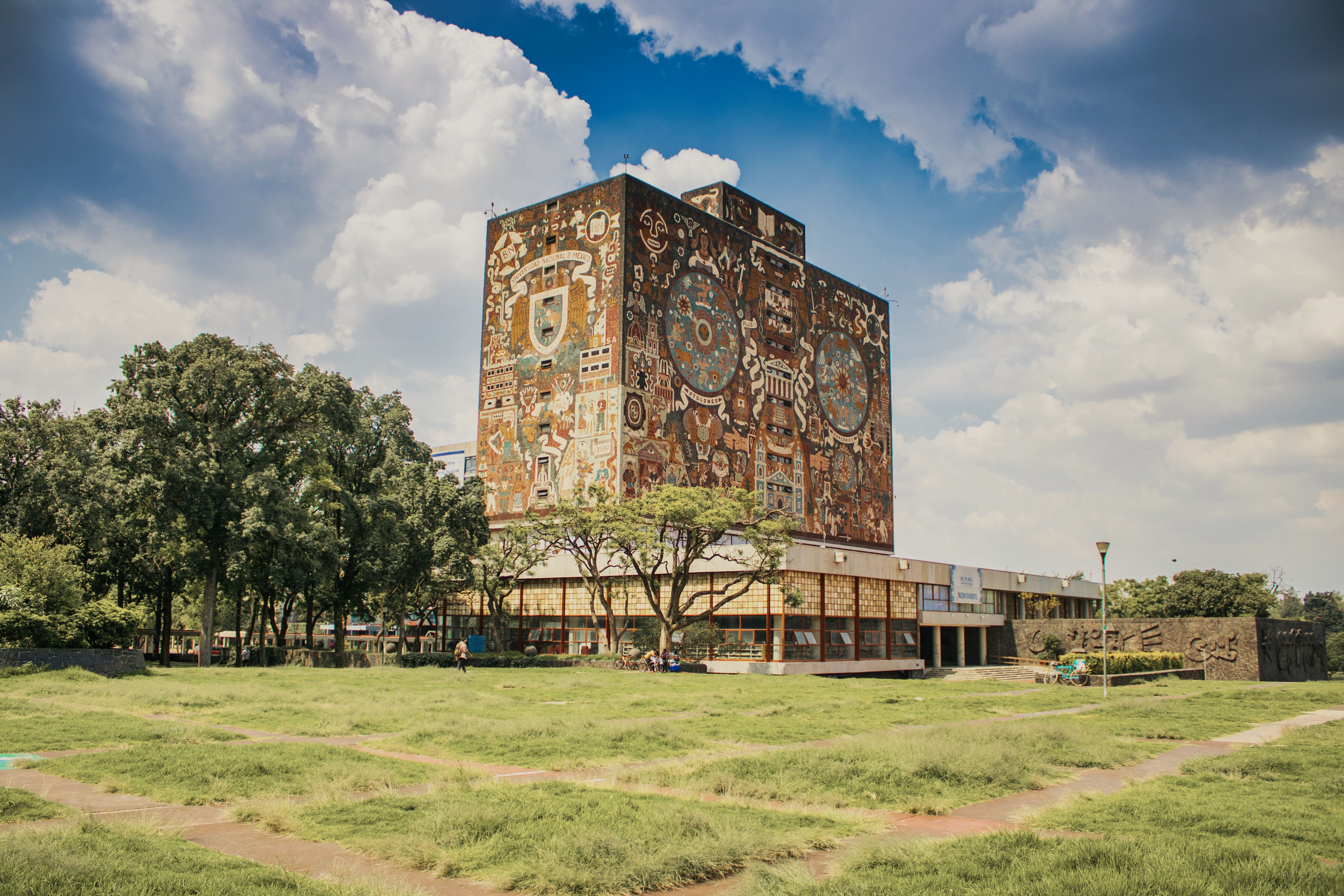 A vibrant mural adorns the iconic UNAM library under a bright blue sky in Mexico City.
