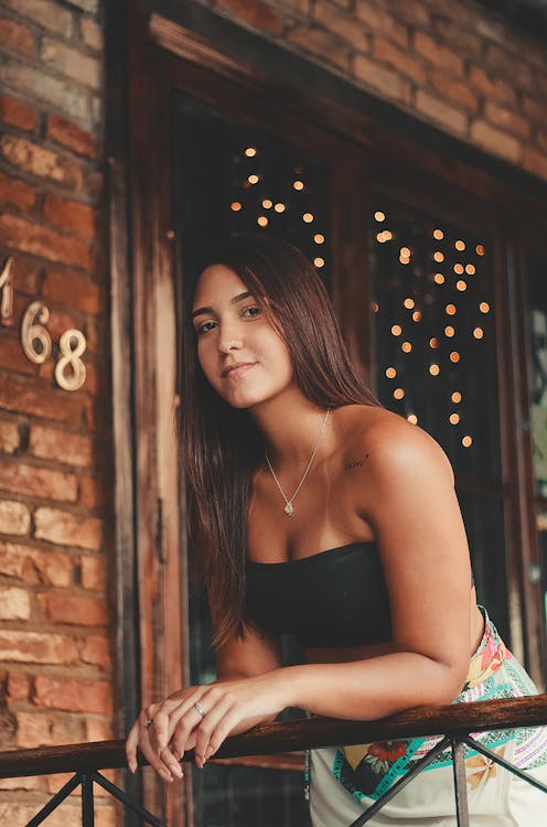 Woman in Black Strapless Crop Top Leaning on Brown Wooden Rail Near Window