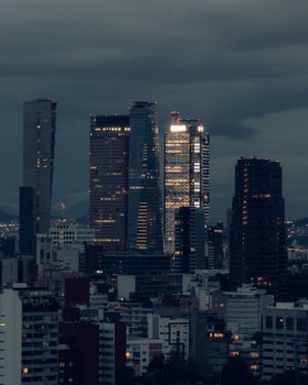 Dramatic nighttime view of Mexico City's skyline with illuminated skyscrapers under a cloudy sky.