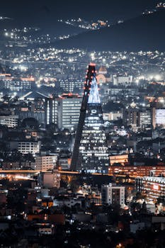 A mesmerizing aerial view of Mexico City's skyline spotlighting the illuminated Torre Insignia at night.