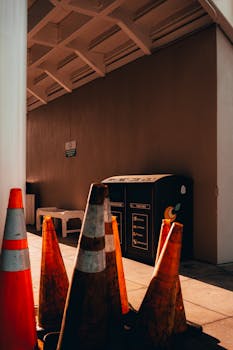 A sunlit urban courtyard with traffic cones and recycling bins, emphasizing city infrastructure.