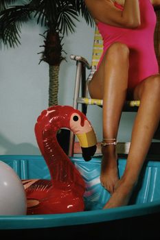 Woman relaxing by a pool with an inflatable flamingo in a tropical setting.