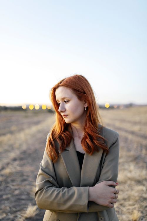 Free Stylish redhead woman wearing a blazer, looking down in an outdoor field Stock Photo