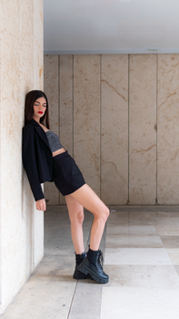 Stylish woman in a black jacket and skirt posing against a marble wall indoors.