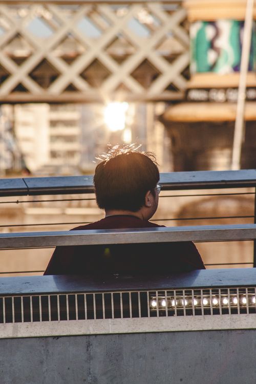 Free A man is sitting on a bridge overlooking the city with sunlight reflecting off the urban structures. Stock Photo