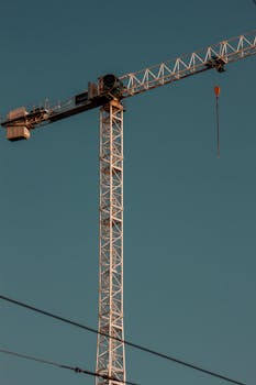 A high tower crane silhouetted against a clear blue sky, ideal for construction themes.