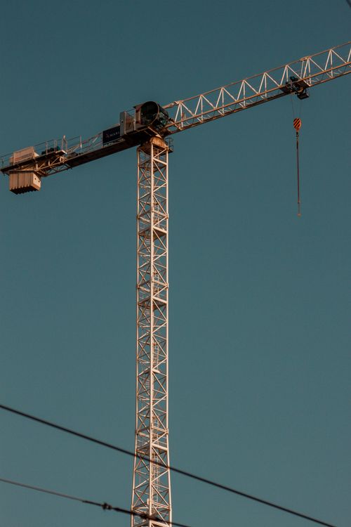 Free A high tower crane silhouetted against a clear blue sky, ideal for construction themes. Stock Photo