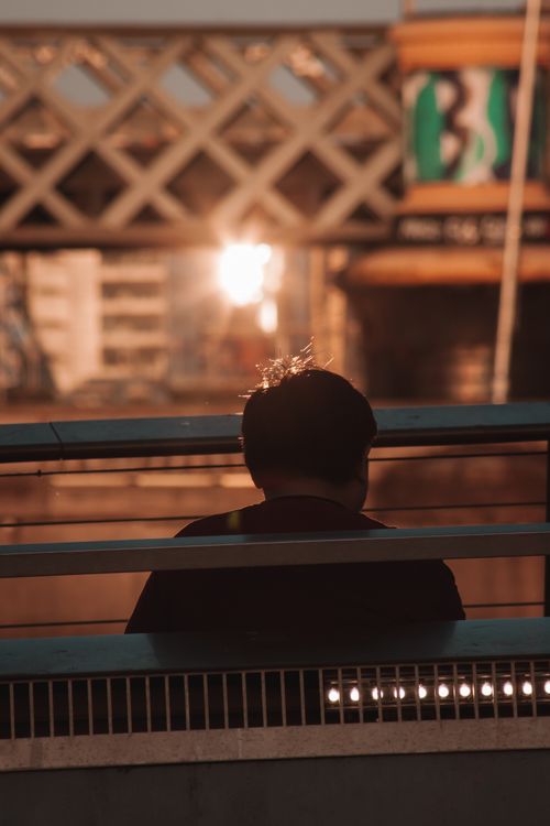 Free Man silhouetted against sunset on a city bridge, capturing urban tranquility and reflection. Stock Photo