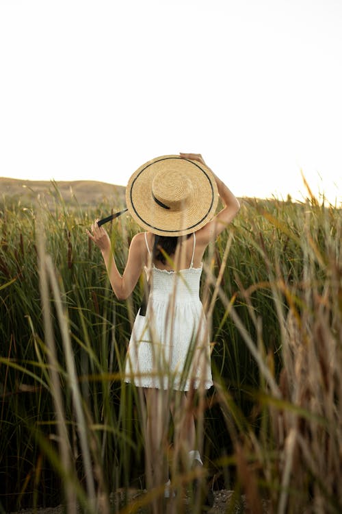 Woman in White Mini Dress and Straw Hat Standing in Reeds