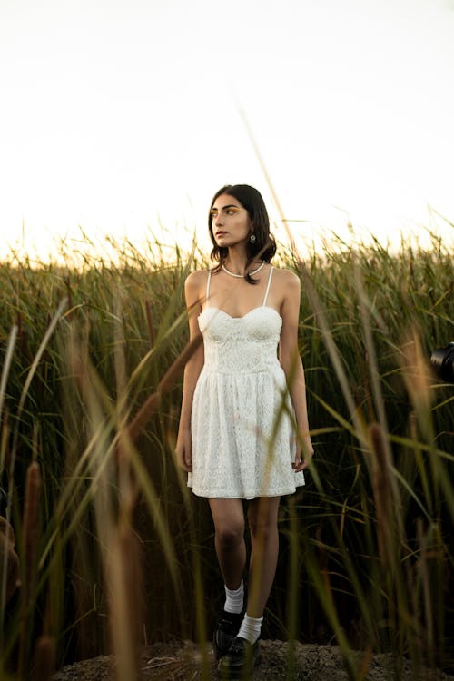 Young Woman in a White Dress Standing on a Grass Field