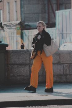 A young woman in vibrant pants walks along a city sidewalk, exuding a casual urban vibe.