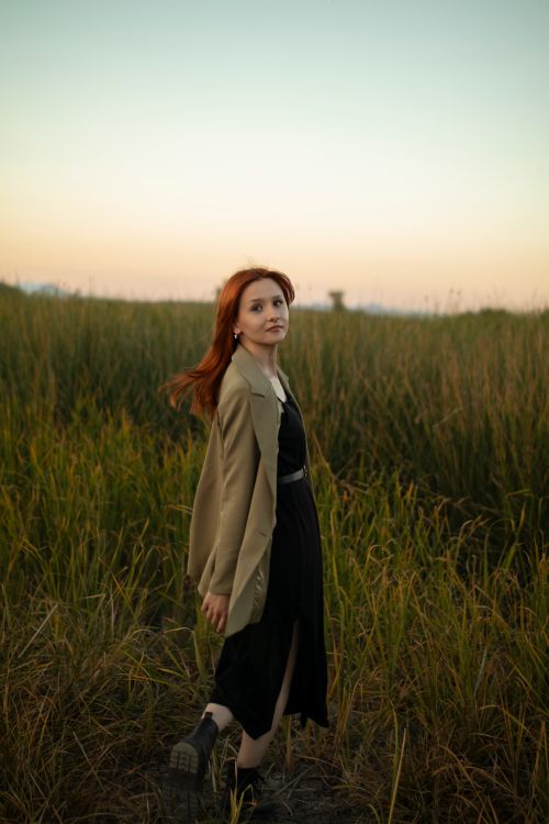 Free Redheaded woman strolling in a grassy field as the sun sets. Stock Photo