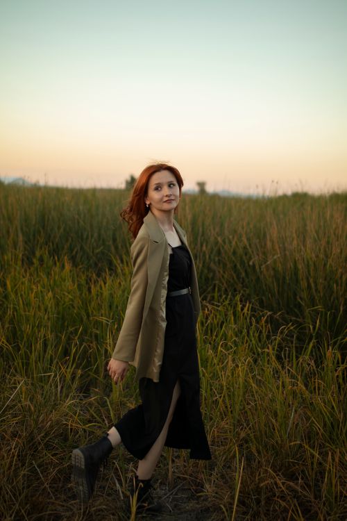 Free Captivating redhead woman walking through a grassy field during sunset, wearing stylish attire. Stock Photo