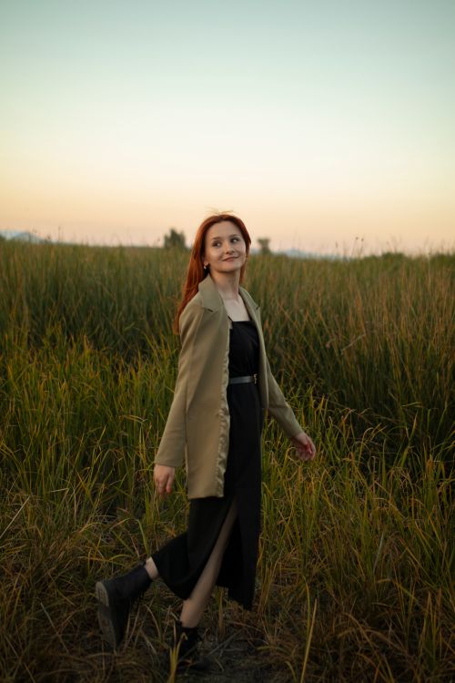 Free Redheaded woman in casual attire walking through a serene field at dusk. Stock Photo