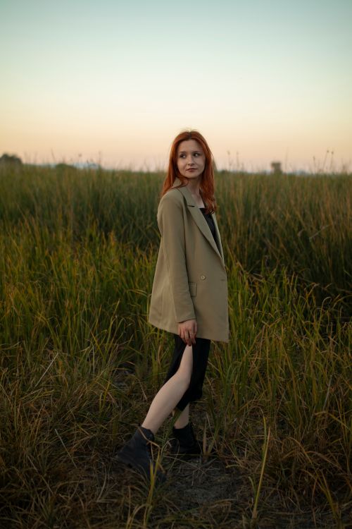 Free Fashionable woman in an open field at sunrise, wearing an olive blazer and black skirt. Stock Photo