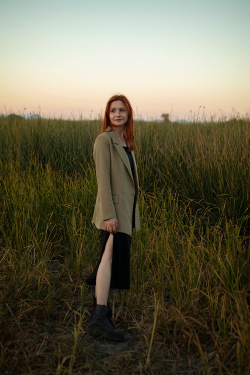 Free Elegant woman in a suit standing in a grassy field at sunset, showcasing fashion and tranquility. Stock Photo