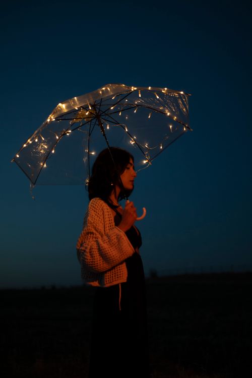 Free A woman stands under an umbrella adorned with lights against a night sky. Stock Photo