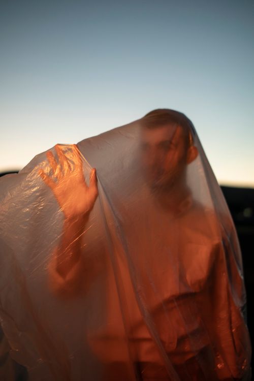 Free A creative portrait capturing a man standing behind translucent fabric illuminated by a warm sunset glow. Stock Photo