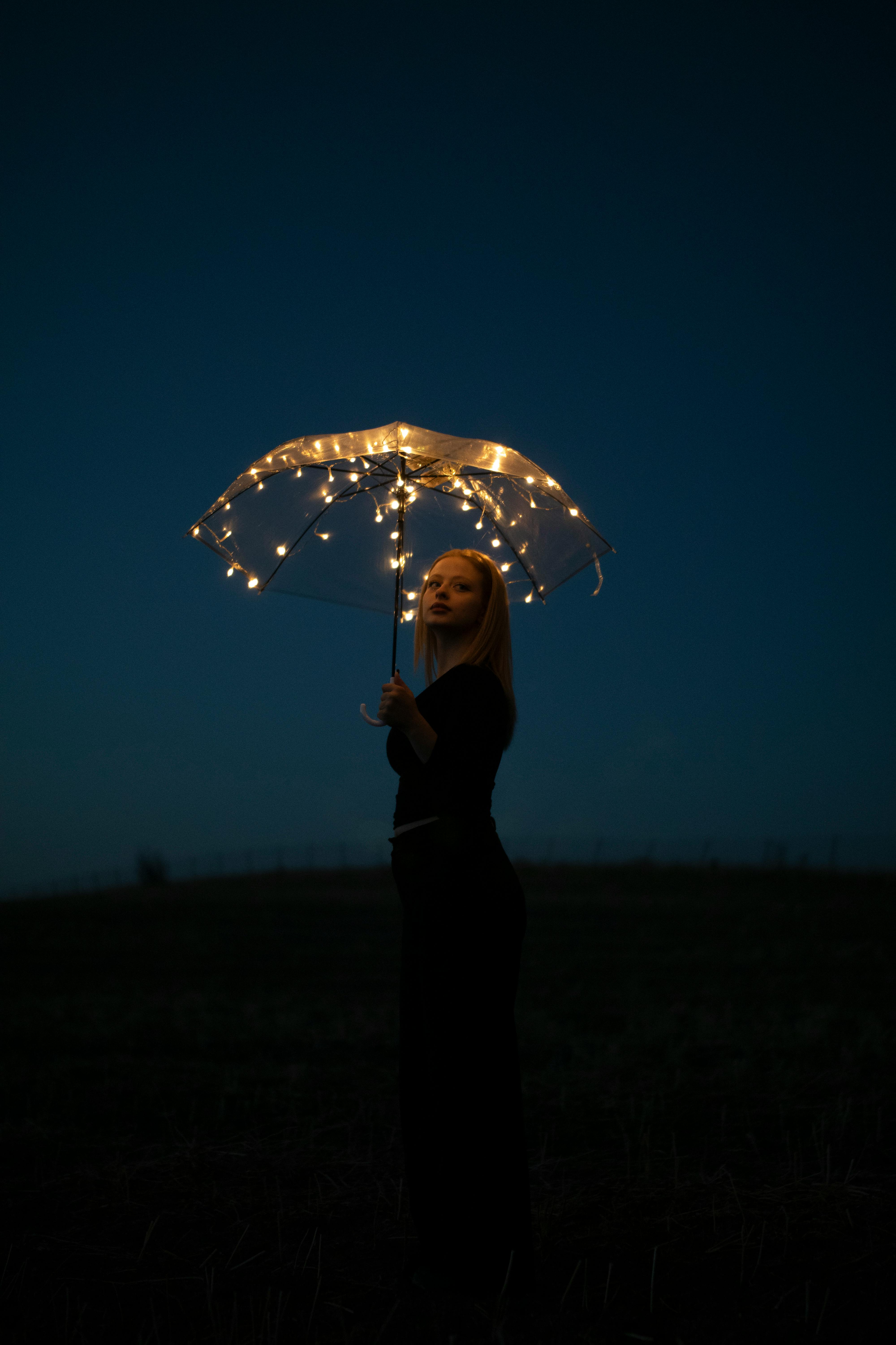 Woman holding an umbrella decorated with lights, creating a glowing effect under the night sky.