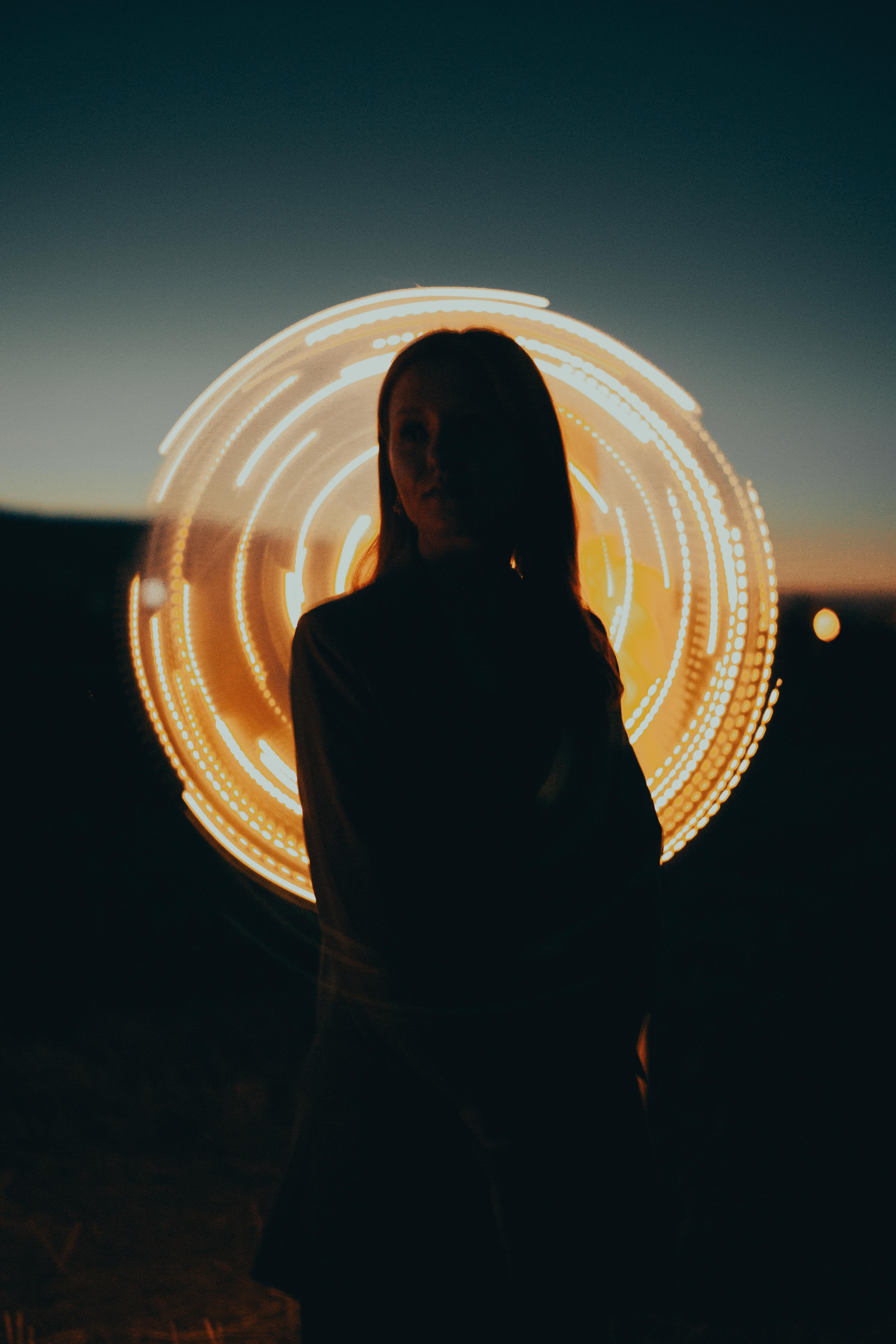 Silhouette of a woman against a backlit circular light pattern at twilight.