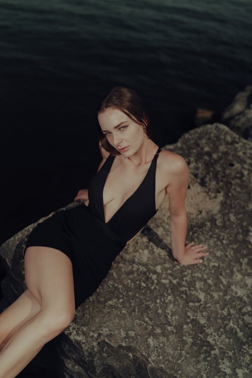 A woman in a black swimsuit sitting on a rock