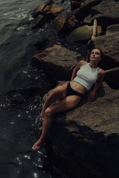A woman in a white top and black shorts laying on rocks