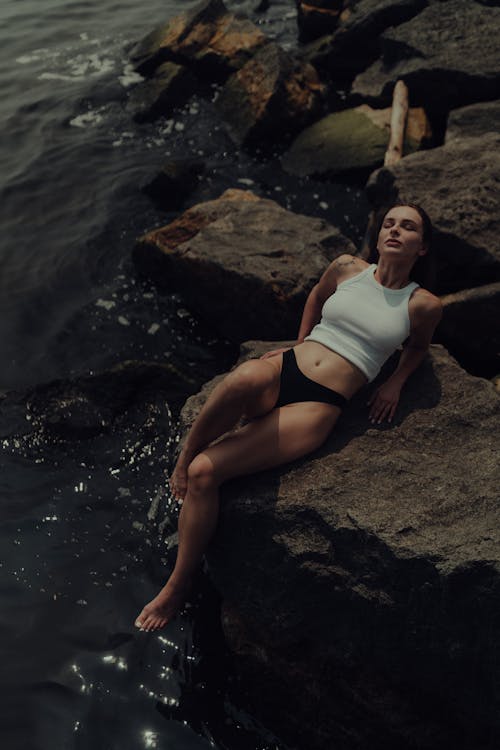 Free A woman in a white top and black shorts laying on rocks Stock Photo