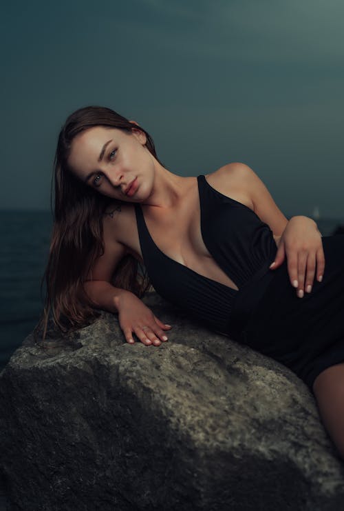 A woman in black dress laying on a rock