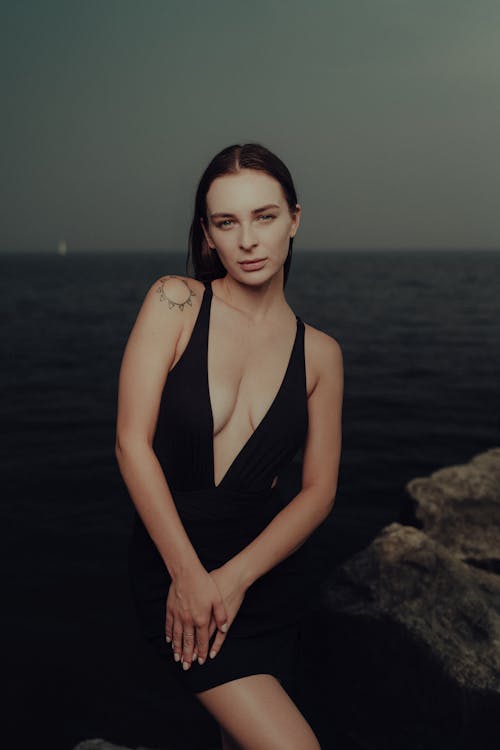 A woman in a black dress posing by the water