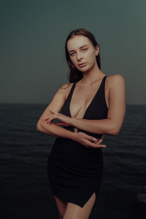 A woman in a black dress posing near the water