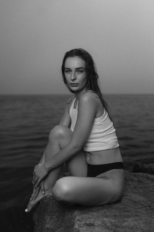 Free A woman sitting on a rock by the water Stock Photo