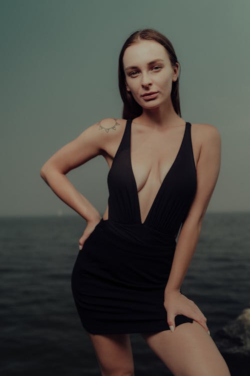 A woman in a black dress posing by the water