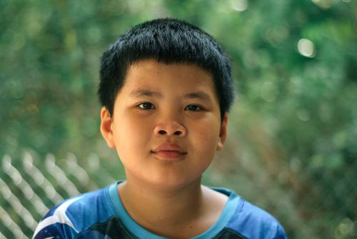 Free A close-up portrait of a young boy with black hair, set against a green outdoor backdrop. Stock Photo