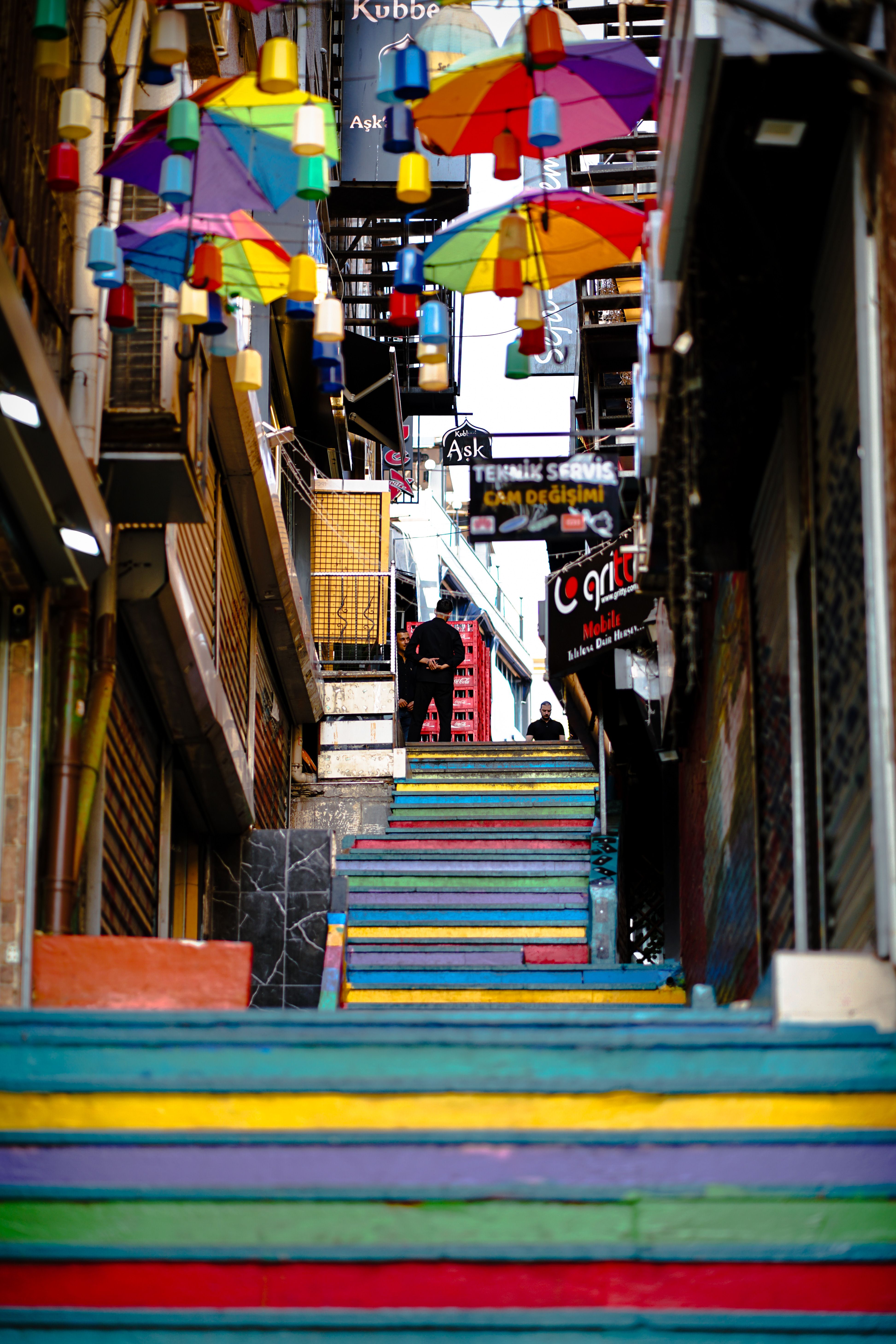 Charming rainbow stairs and hanging umbrellas in Balat, Istanbul, create a vibrant urban scene.
