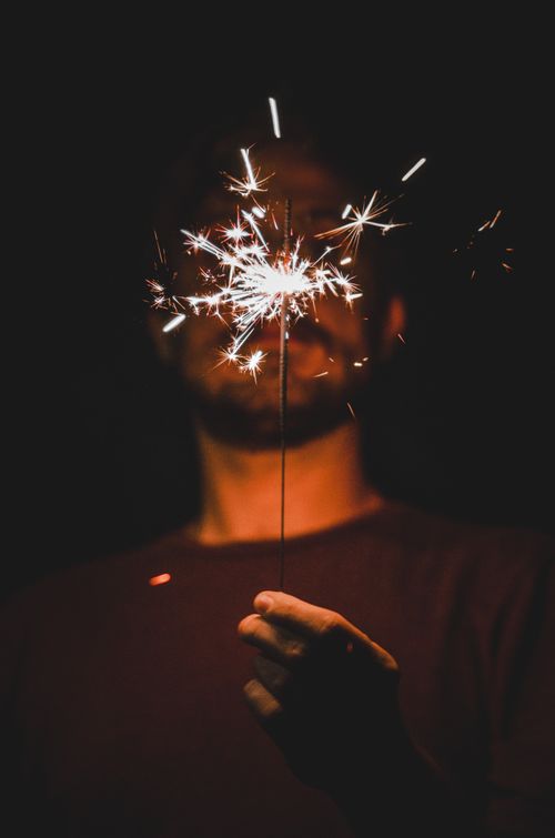 Free A man illuminates the night with a sparkler, creating a warm, festive glow. Stock Photo