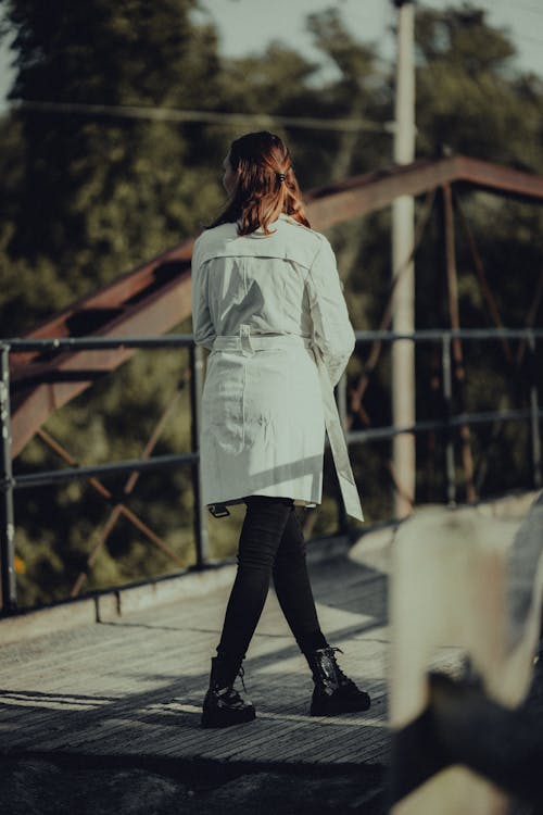 Woman in White Coat Walking on Footbridge