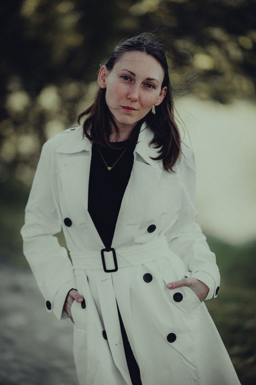 Free Portrait of a woman wearing a stylish white trench coat standing outdoors with a serene expression. Stock Photo